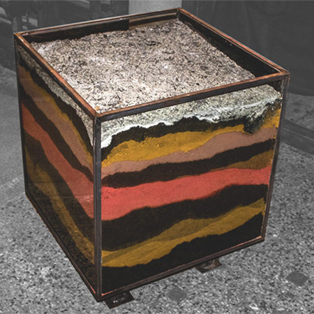 Qudratische Glasbox gefüllt mit mehrfarbigen Erdschichten